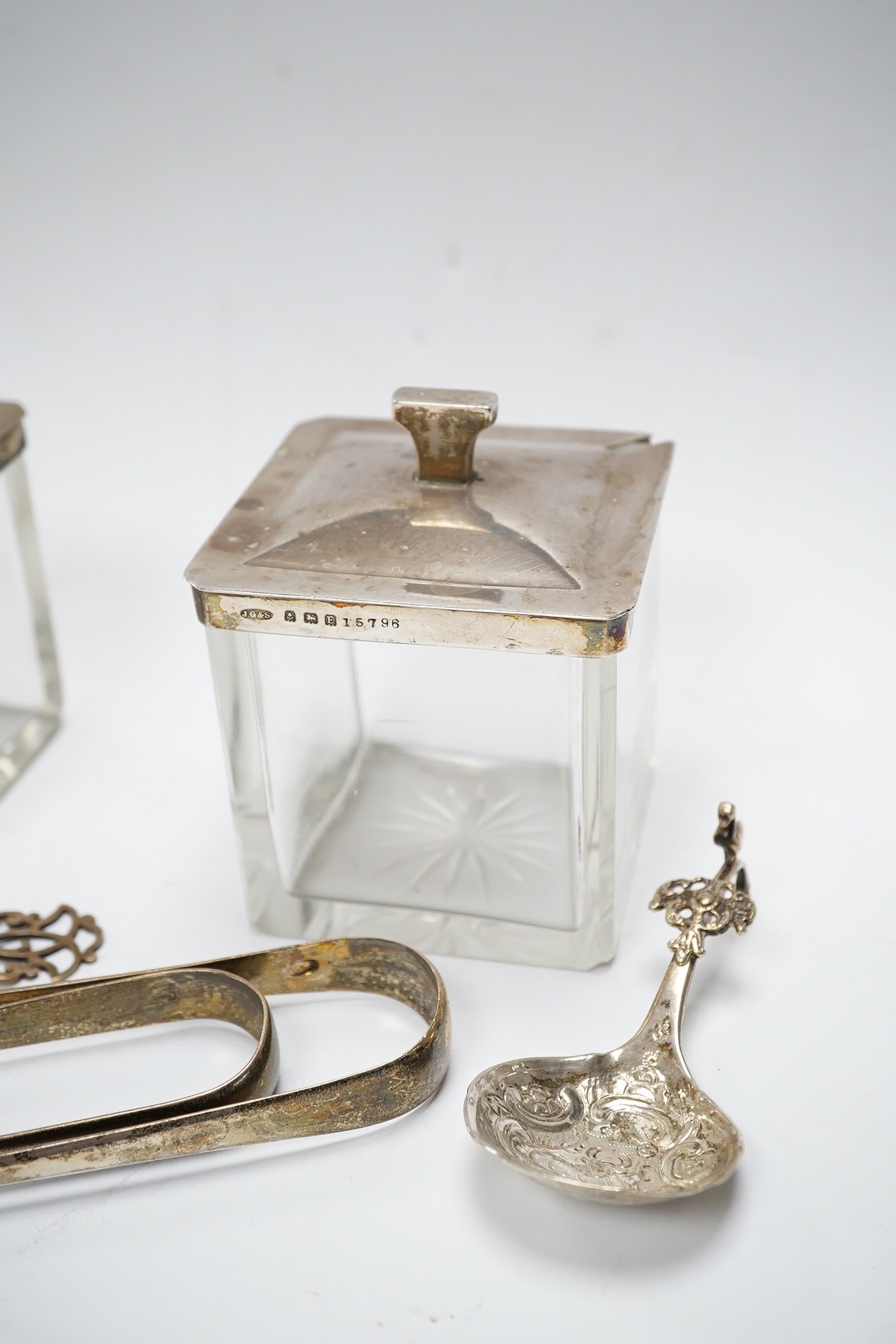 Two square silver topped glass preserve pot, two pairs of George III silver sugar tongs, a silver tea strainer and a caddy spoon. Condition - fair